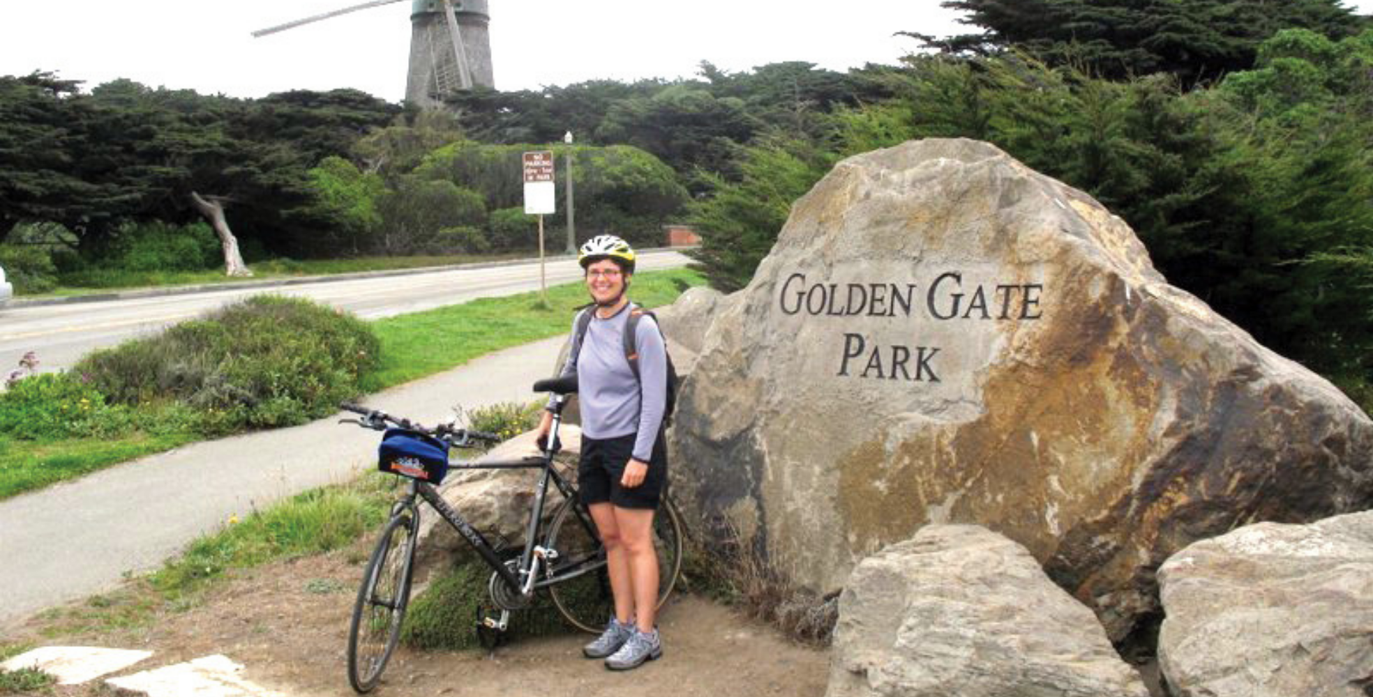 woman standing next to bike rental and golden gate park sign on boulder